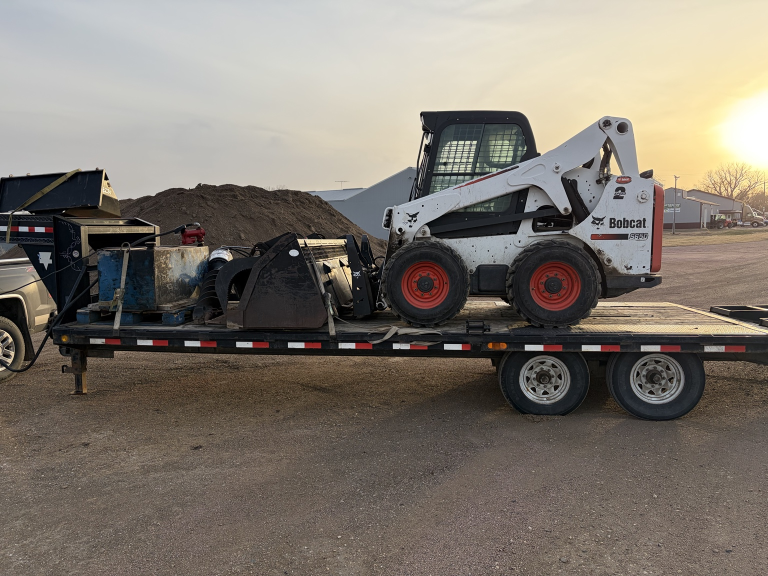 Bobcat and stump grinding equipment loaded on trailer at sunset in Marshall, Minnesota